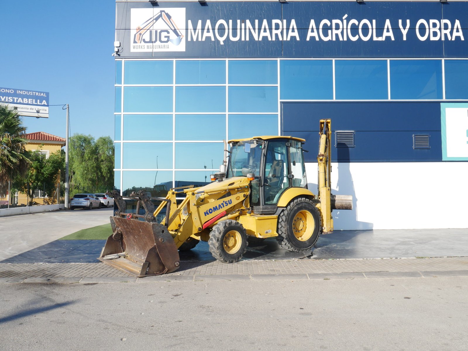 Retroexcavadora Komatsu WB97R-5 con pinzas porta palets, cazo almeja y mandos pilotados trabajando en obra