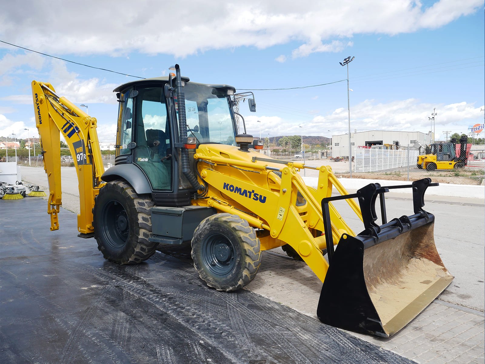 Komatsu WB97R año 2007 con 18.000 horas y matriculada. Retroexcavadora con A/A, pinzas porta palets, enganche rápido y cazo 40 cm. Disponible en JJG Works con envío a toda España.